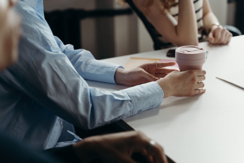 Close-up of people holding a coffee cup during a casual business meeting indoors.
