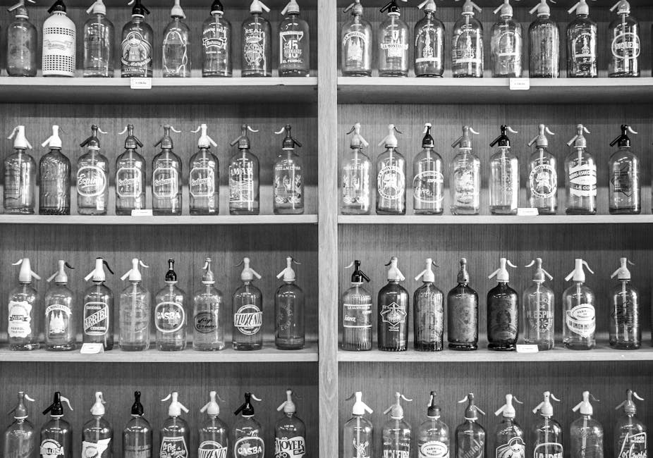 Black and white photo showcasing a collection of vintage seltzer bottles on wooden shelves.