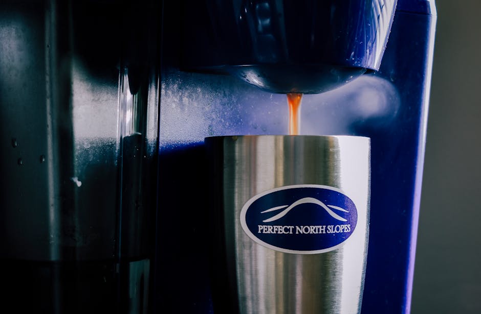 Stainless steel cup with coffee pouring from a coffee machine indoors.