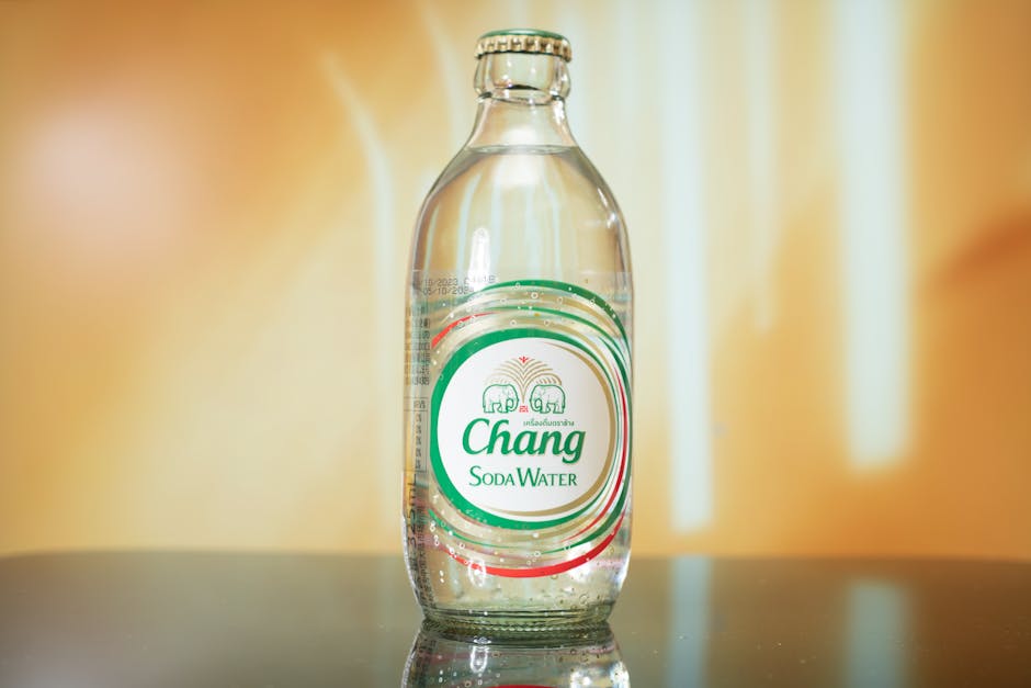 A clear Chang soda water bottle with label on a reflective table indoors.