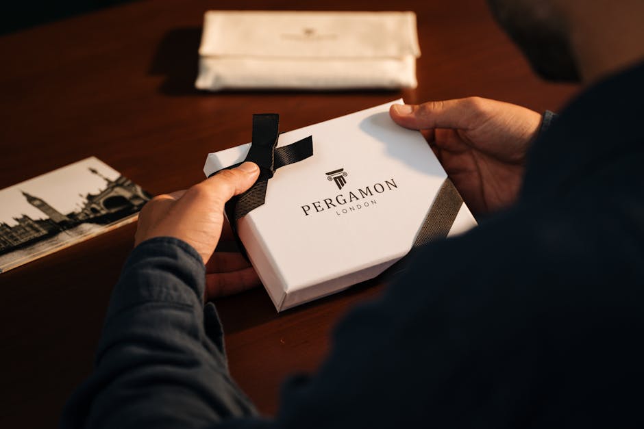Hands holding a Pergamon London gift box on a wooden table, creating an elegant unboxing theme.