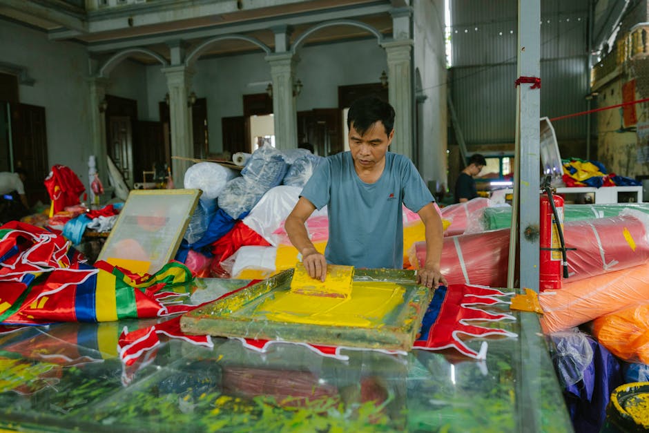 A man engaged in screen printing vibrant textiles inside a workshop filled with colorful materials.