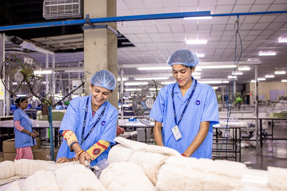 Smiling Indian factory workers in a textile factory wearing blue uniforms and hairnets, working diligently.