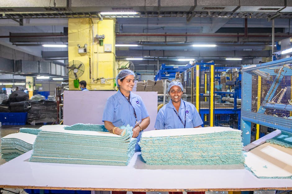 Two female textile workers in uniform operate in a bustling modern factory interior.